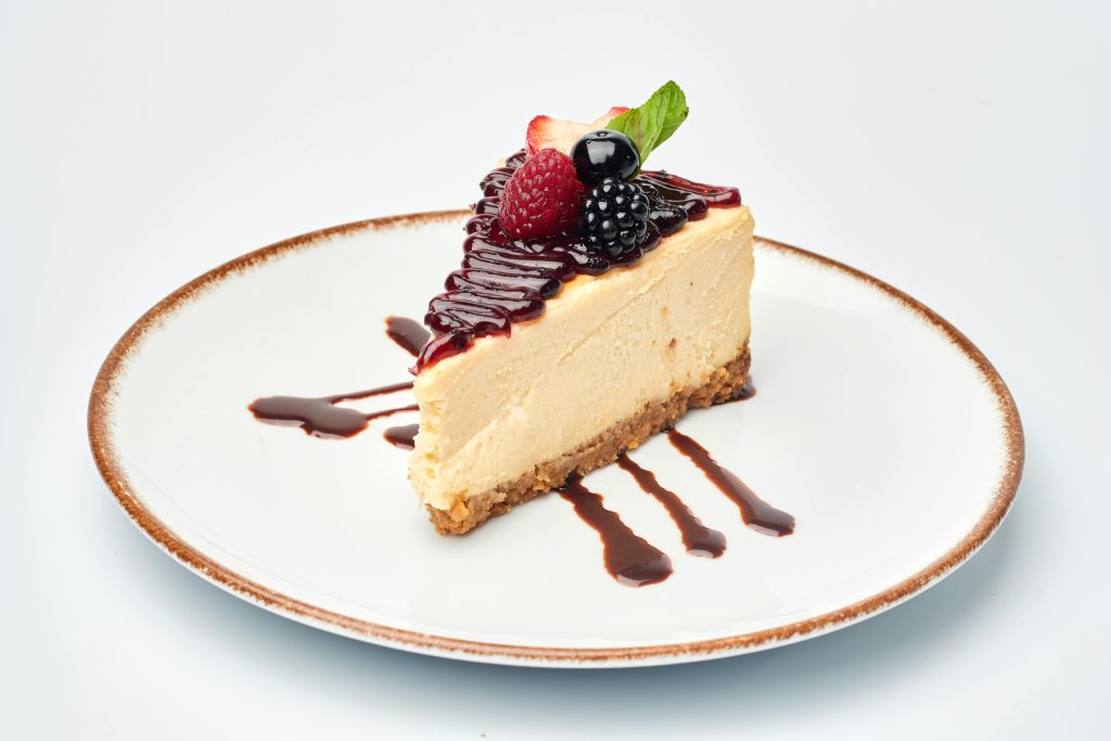 A slice of creamy cheesecake topped with fresh berries and chocolate drizzle.