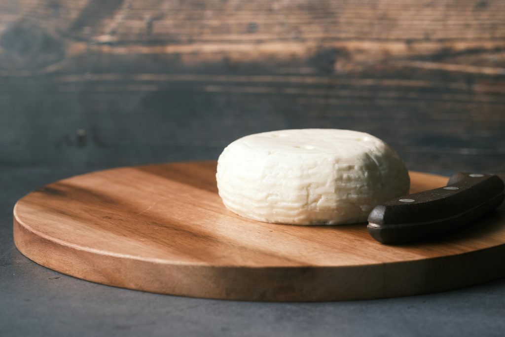 Round cheese on a rustic wooden board with a knife, depicting simplicity and gourmet appeal.